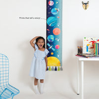 Child standing next to a colorful growth chart with space-themed design.