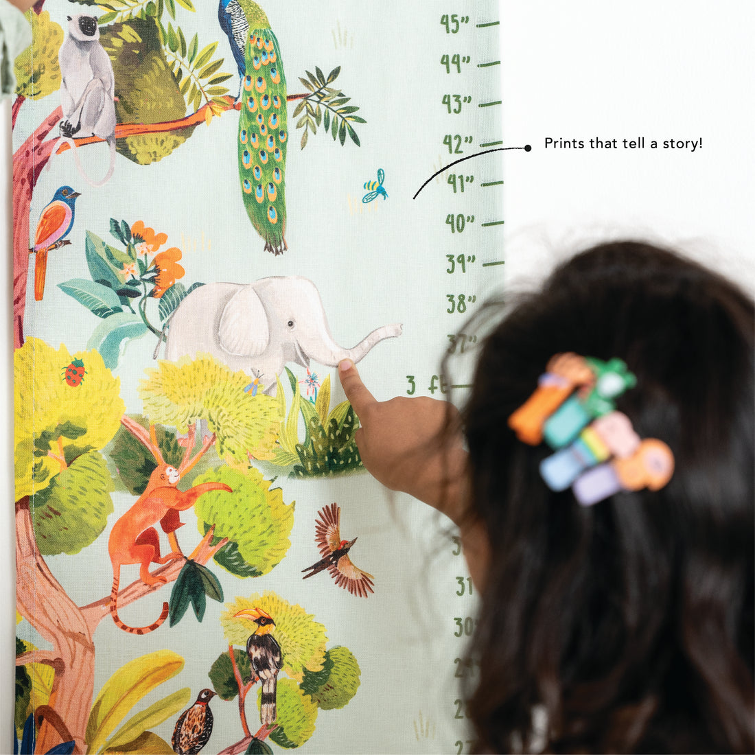 Child pointing at a colorful jungle-themed growth chart with animals and trees.