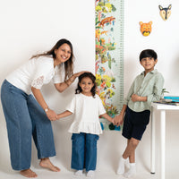 Family of three with a child standing next to a growth chart, with a child's toy tiger on the wall.
