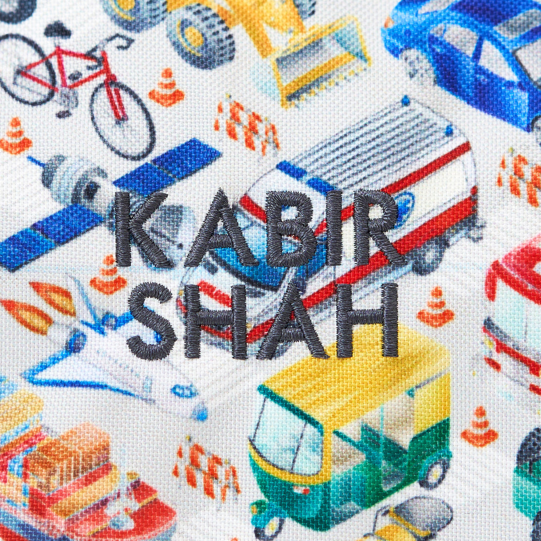 Text 'KABIR SHAH' on fabric with colorful vehicle illustrations