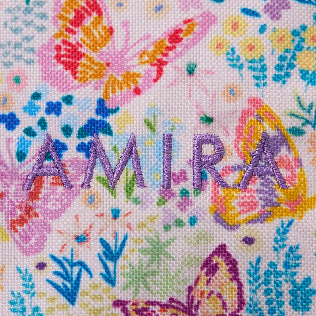 Embroidered name 'AMIRA' on a floral background with colorful flowers and leaves.