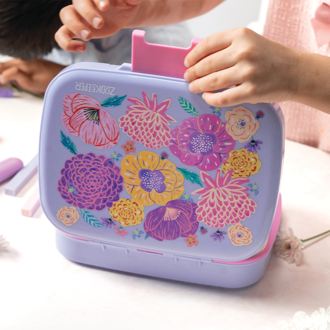 Floral-patterned purple case with pink top held by a child's hand on a light background