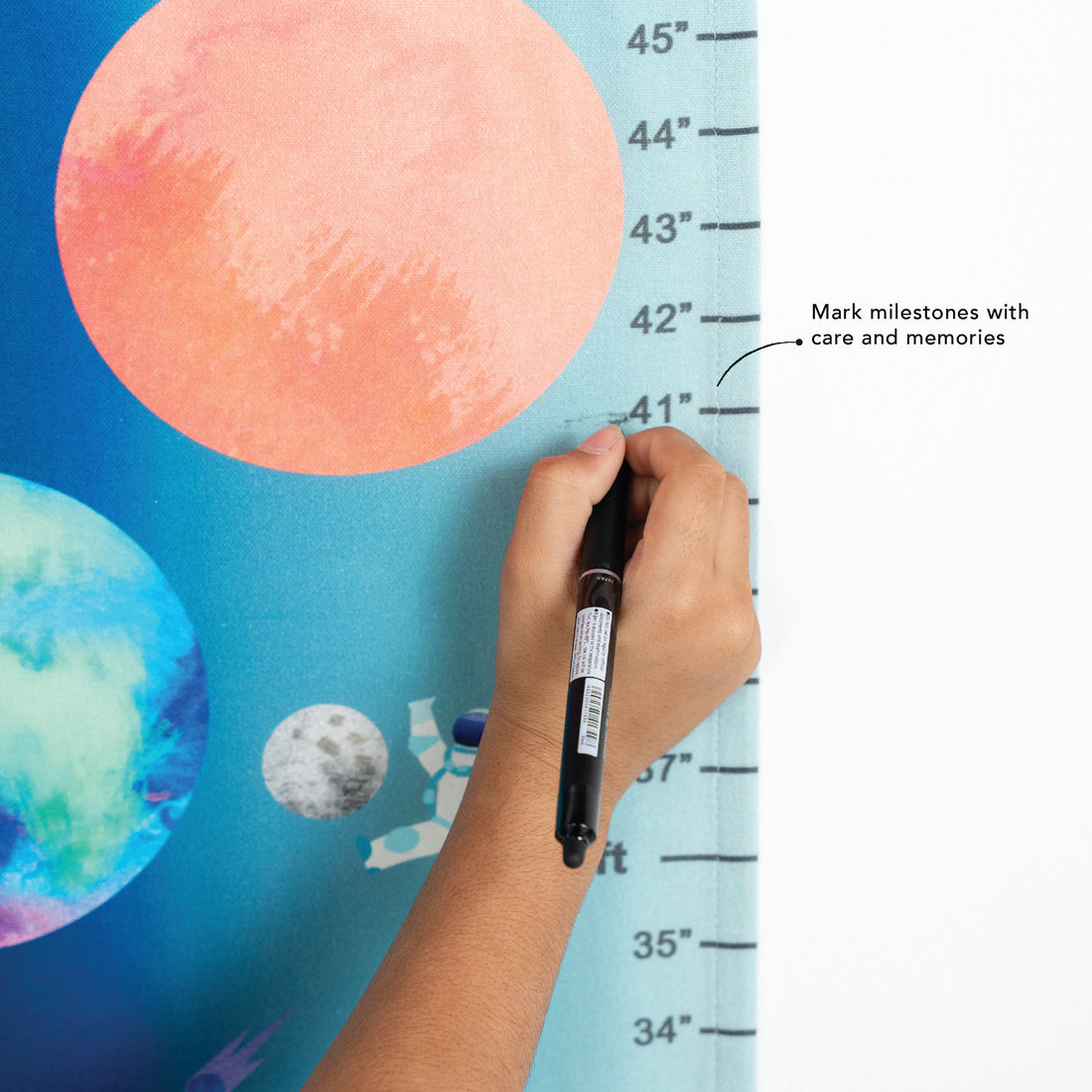 Hand holding a marker near a colorful space-themed height chart with a ruler.