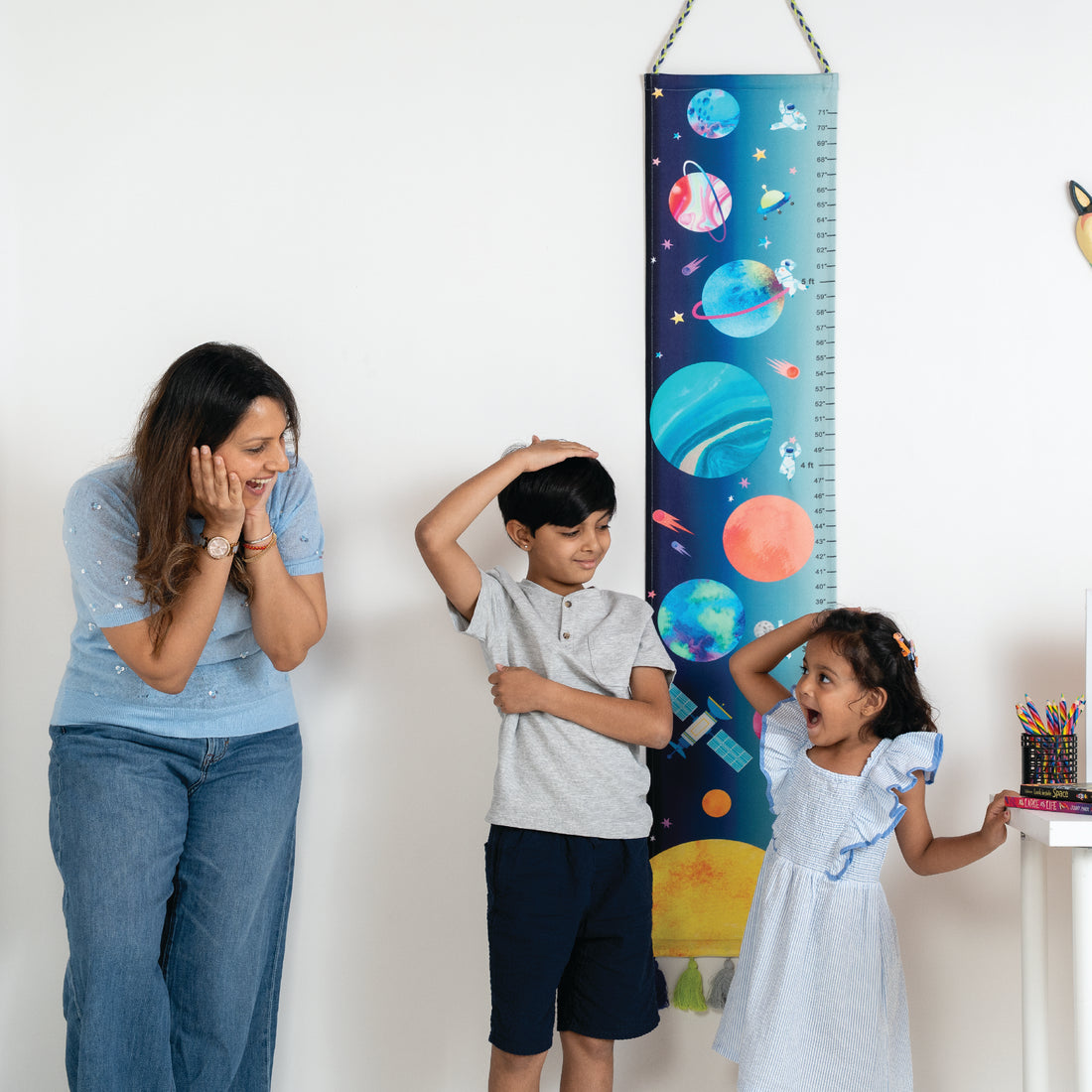 Woman and two children measuring height against a colorful growth chart with space-themed design.